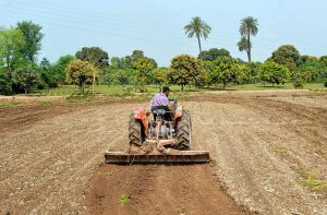 A farmer prepares his agricultural land with the help of a tractor for the cultivation of the next crop at a farmland on the outskirts of the city.