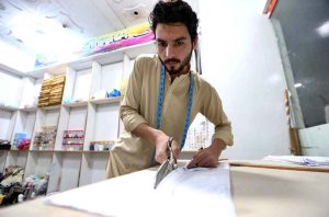 Tailor busy cutting and stitching clothes for customers at his workplace in connection with upcoming Eid-ul Fitr.