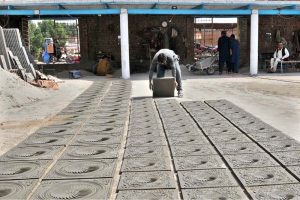 A worker busy preparing decorative cement tiles at a local factory, laying freshly molded in rows to dry under the sun before supply to the market.