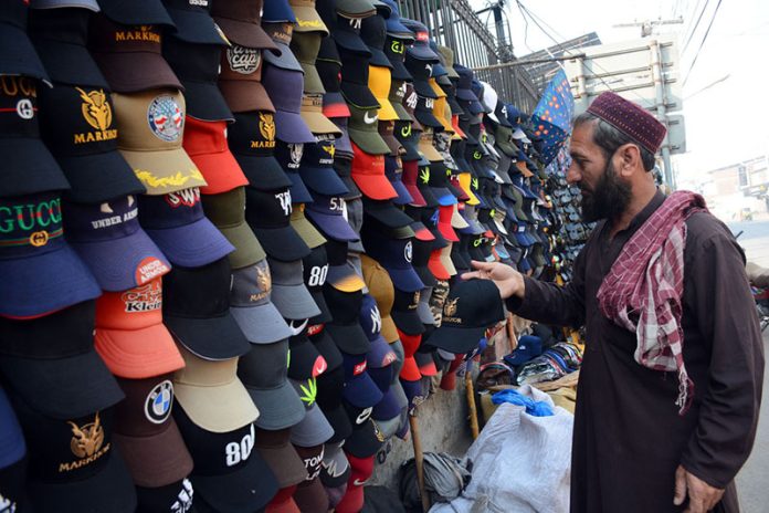 A vendor displaying and selling caps to the customers at his roadside setup