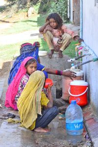 Gypsy girls are filling their pots with clean water from a tap in Husseinabad