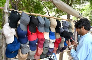 A passerby selecting cap from a stall along the roadside.