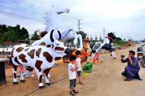 A person photographs his children with replica animal models displayed by a vendor along the roadside in Qasimabad.