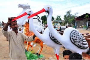 A person photographs his children with replica animal models displayed by a vendor along the roadside in Qasimabad.