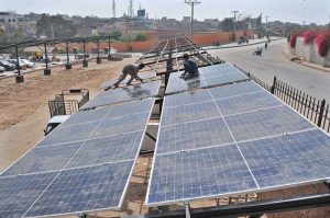 Workers are busy installing solar panels on a roadside structure to generate renewable energy and provide shade for vehicles.