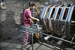 A worker supervises embroidery design work on fabric using a computerized embroidery machine at a local factory.