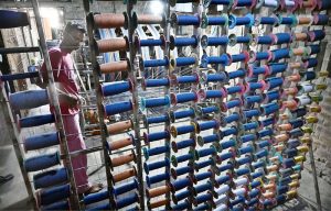 A worker supervises embroidery design work on fabric using a computerized embroidery machine at a local factory.