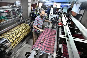 A worker supervises embroidery design work on fabric using a computerized embroidery machine at a local factory.