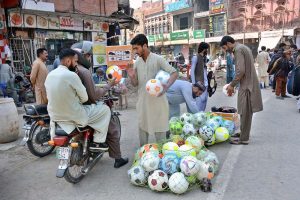 A vendor displaying and selling football to customer at his roadside stall.