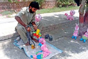 A vendor fills air in toys using hand pump at his roadside setup.