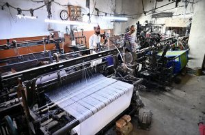 A worker supervises embroidery design work on fabric using a computerized embroidery machine at a local factory.