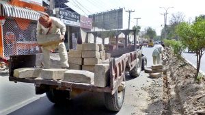 A labourer busy unloading cemented blocks from tractor-trolley for fixing at center path of road.