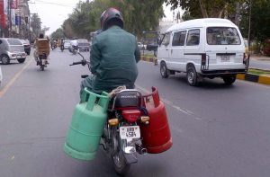 A man carries two large cylinders on a motorcycle, creating a potential traffic hazard.