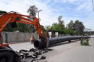 A heavy excavator breaks the road surface as workers prepare to install a large pipeline along the roadside in the Shamsabad area of the city.