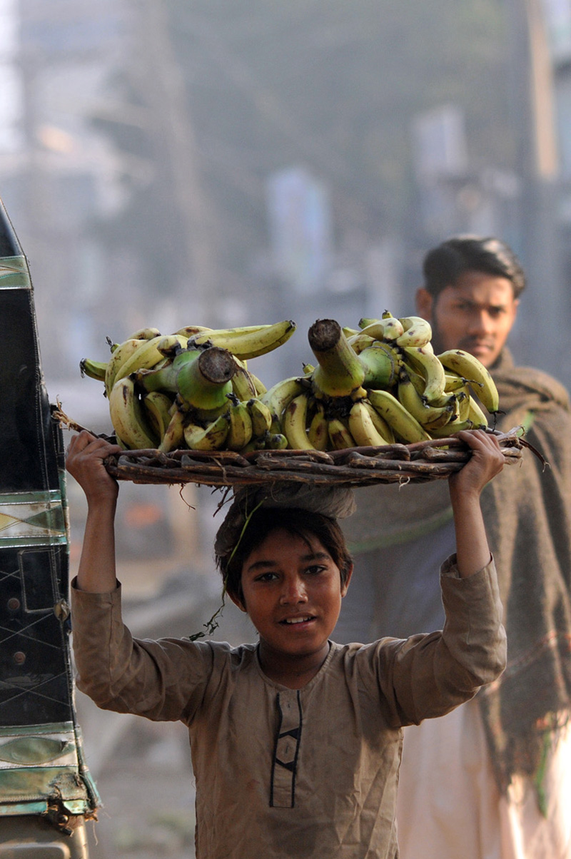 A young laborer carries a basket of bananas on his head during an auction as shopkeepers place bids at the fruit market