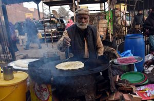 An elderly vendor preparing Saag Paratha to attract customers at his roadside setup.