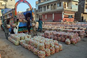 A young laborer carries a basket of bananas on his head during an auction as shopkeepers place bids at the fruit market