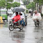 Motorcyclists under the cover of umbrella and polythene sheet on their way during light rain in the city