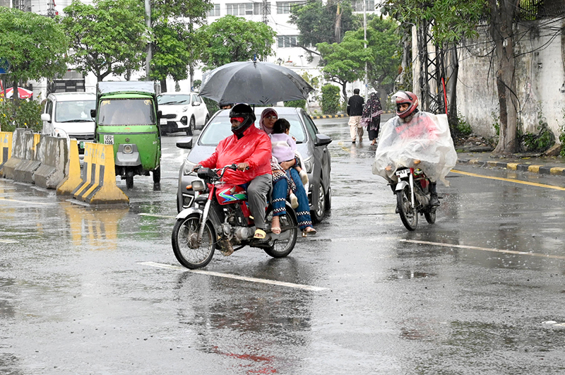 Motorcyclists under the cover of umbrella and polythene sheet on their way during light rain in the city