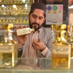 A vendor fills small rolling bottles while selling a variety of perfumes and fragrances at Hashtnagri area