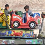 Children have fun on a swing set along the roadside, enjoying the playful moment.