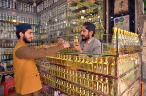 A vendor fills small rolling bottles while selling a variety of perfumes and fragrances at Hashtnagri area