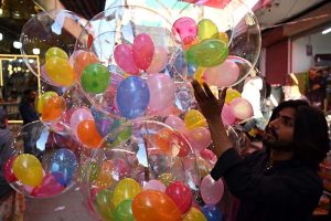 A vendor sells colorful balloons at Resham Gali while striving to support his family.