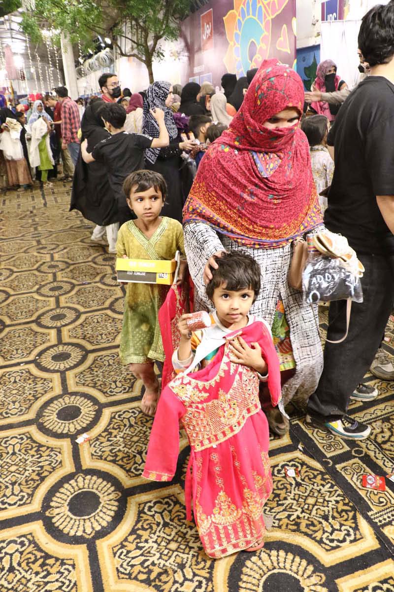A mother along with her children is expressing joy by selecting Eid dresses of their choice on Chand Raat at the Eid Free Bazaar 'Maa Hum Bhi Eid Manyen Gay,' organized by the JDC Welfare Foundation