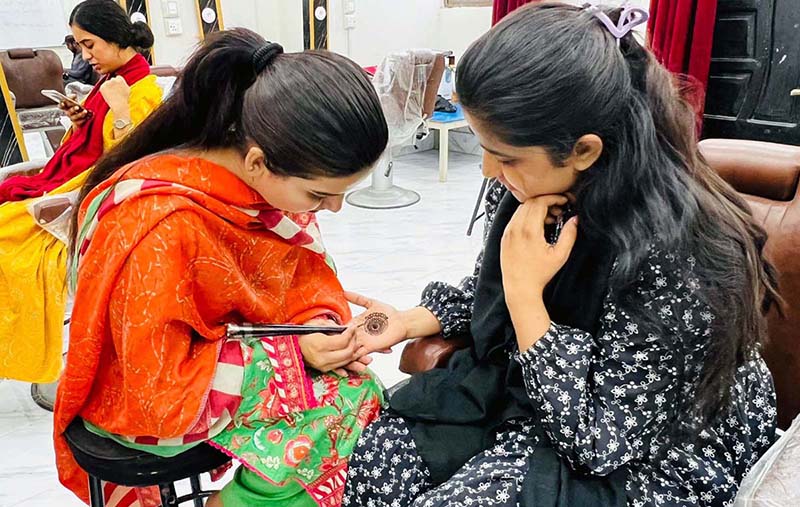A female worker applies mehndi on a woman’s hand at a beauty salon in Resham Gali ahead of Eid-ul-Fitr