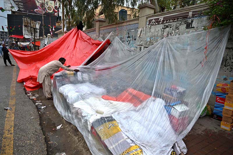 A vendor covers his roadside stall near the Girls College with a plastic sheet to protect it from the rain that the city is experiencing