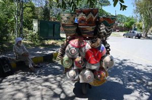 An elderly vendor displays household items on his bicycle while waiting for customers along a roadside near the I-8 area in the Federal Capital