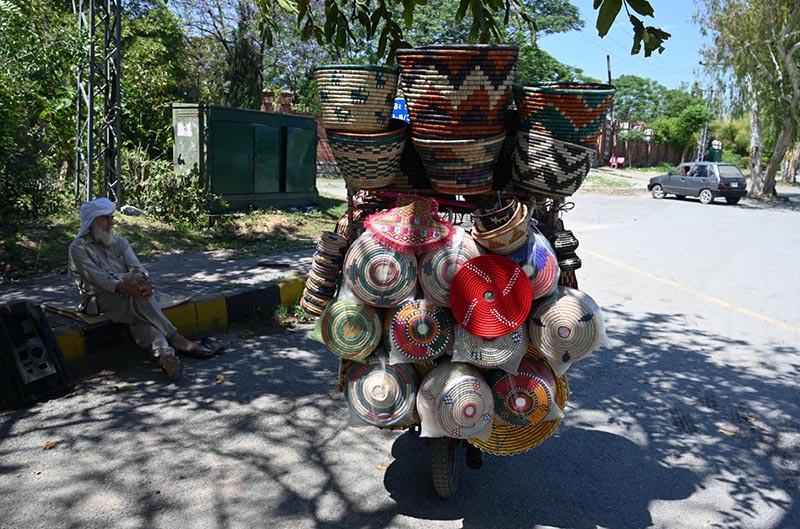 An elderly vendor displays household items on his bicycle while waiting for customers along a roadside near the I-8 area in the Federal Capital