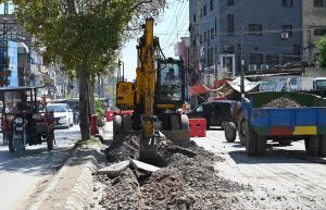 A worker operates heavy machinery to dig a trench for laying an underground water supply line in Khayaban-e-Sir Syed
