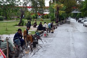 Daily-wage laborers wait for customers with their tools while sitting along the roadside near the G-8 area in the Federal Capital