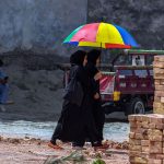 Two girls walk past while sharing a multi-colored umbrella to protect themselves from the heat and sun near Ghouri town area