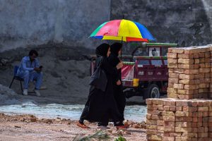 Two girls walk past while sharing a multi-colored umbrella to protect themselves from the heat and sun near Ghouri town area