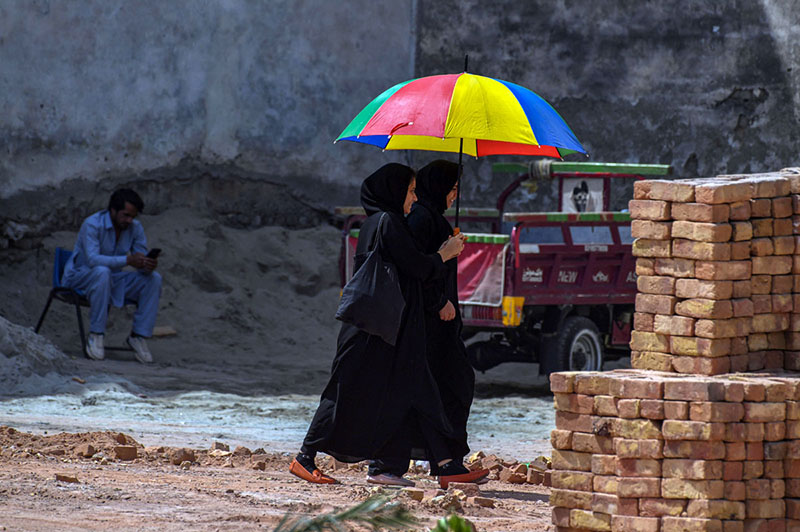 Two girls walk past while sharing a multi-colored umbrella to protect themselves from the heat and sun near Ghouri town area