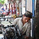 A young mechanic repairing a car engine at a roadside workshop near Pirwadhai area in the city