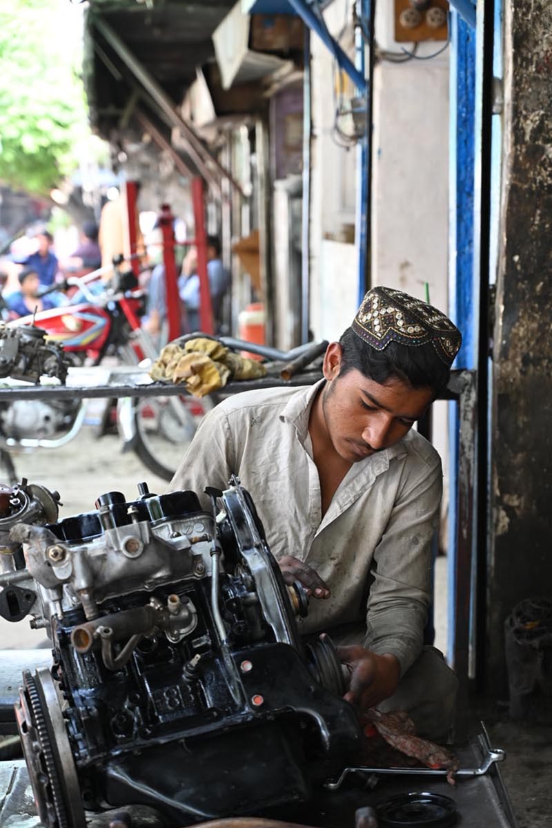 A young mechanic repairing a car engine at a roadside workshop near Pirwadhai area in the city