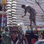 Labourers unload sacks of sugar from a decorated truck. Manual labor remains essential to the supply chain as the government works to regulate commodity prices