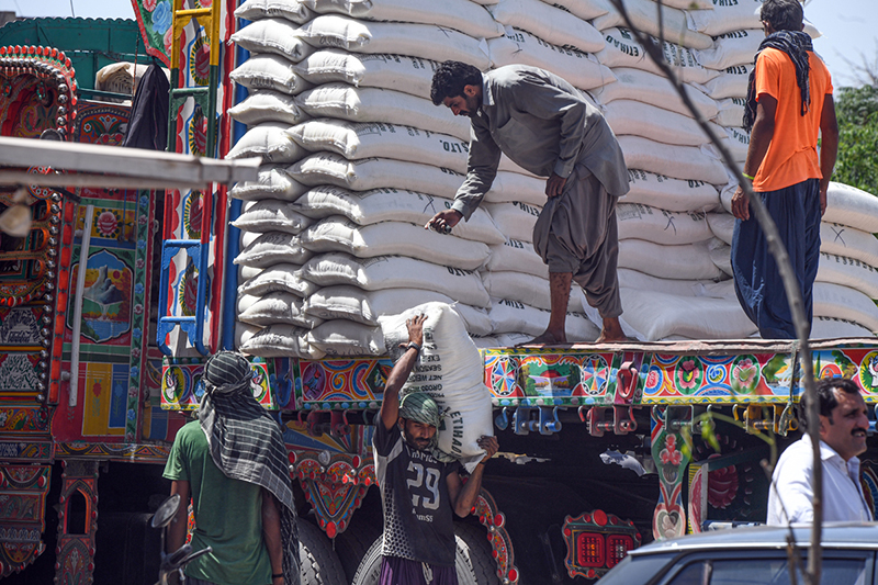 Labourers unload sacks of sugar from a decorated truck. Manual labor remains essential to the supply chain as the government works to regulate commodity prices