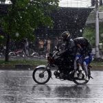 Students ride with their father on a motorcycle, covered with a plastic sheet, while heading to school during heavy rain on the Expressway in the Federal Capital