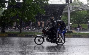 Students ride with their father on a motorcycle, covered with a plastic sheet, while heading to school during heavy rain on the Expressway in the Federal Capital