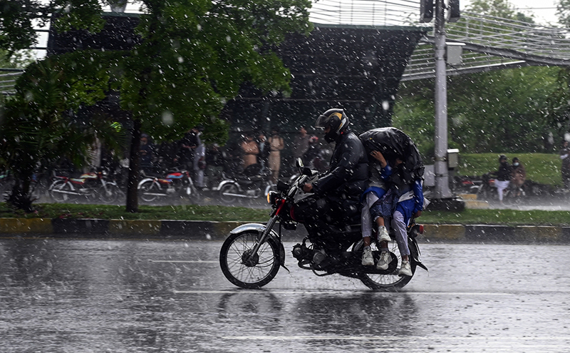 Students ride with their father on a motorcycle, covered with a plastic sheet, while heading to school during heavy rain on the Expressway in the Federal Capital