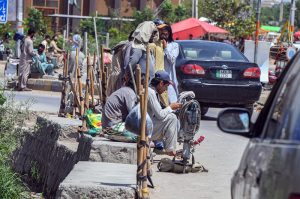 Daily-wage laborers sit along a roadside with their specialized tools, including jackhammers and picks, as they wait for potential employers to offer construction or renovation work at Tarlai area