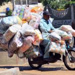 A motorcyclist rides through stagnant rainwater after rainfall while carrying bags of chips on his way in Latifabad