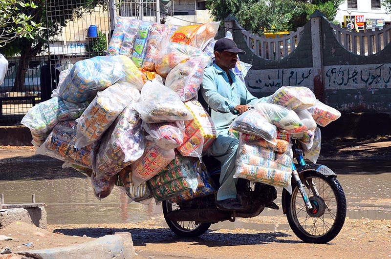 A motorcyclist rides through stagnant rainwater after rainfall while carrying bags of chips on his way in Latifabad