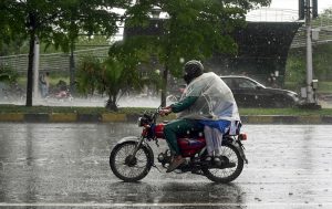 Students ride with their father on a motorcycle, covered with a plastic sheet, while heading to school during heavy rain on the Expressway in the Federal Capital