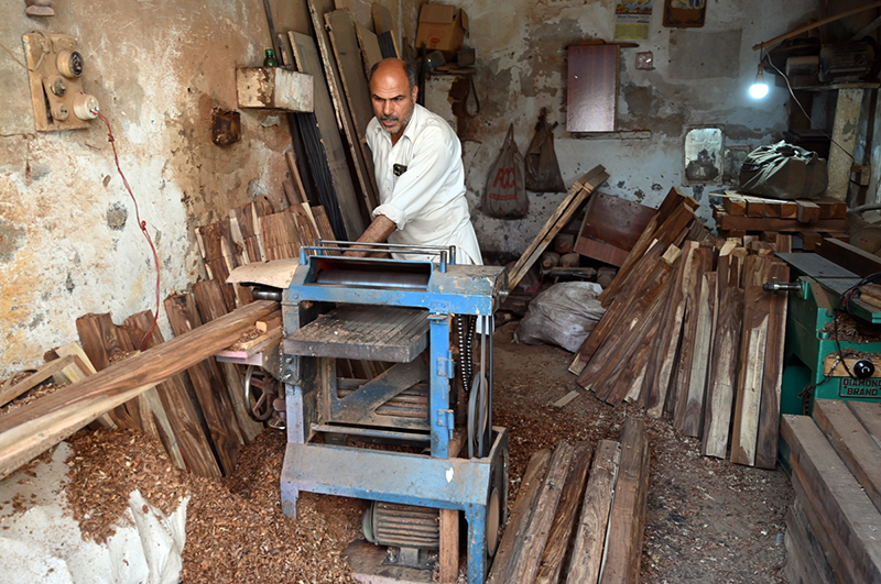 A woodworker guides a slab of raw timber through a surface planer in a local carpentry shop, where raw materials are transformed into finished products for the domestic market