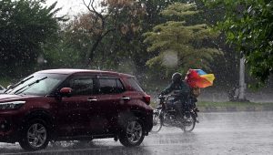 Students ride with their father on a motorcycle, covered with a plastic sheet, while heading to school during heavy rain on the Expressway in the Federal Capital